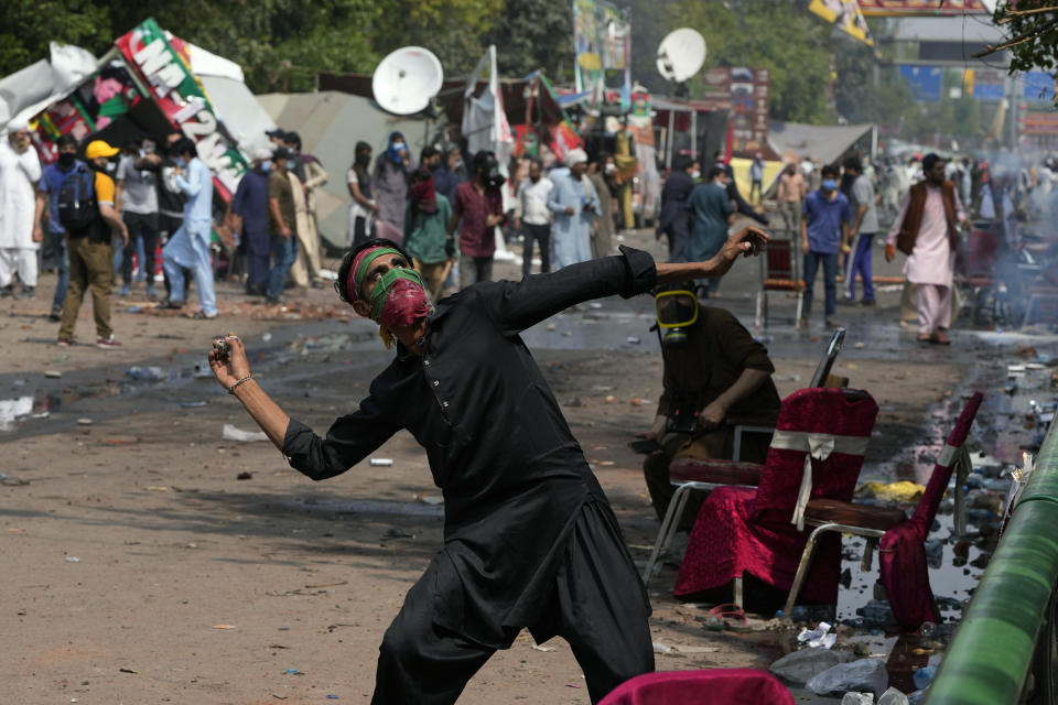 A supporter of former Prime Minister Imran Khan throws a stone towards riot police officers, during clashes, in Lahore, Pakistan, Wednesday, March 15, 2023. Pakistani police have paused efforts to arrest former Prime Minister Imran Khan on graft charges after clashes continued for a second day outside his home in the eastern city of Lahore. (AP Photo/K.M. Chaudary)