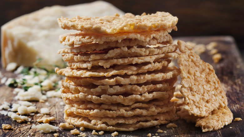 a stack of parmesan crisps on a cutting board with a wedge of parmesan