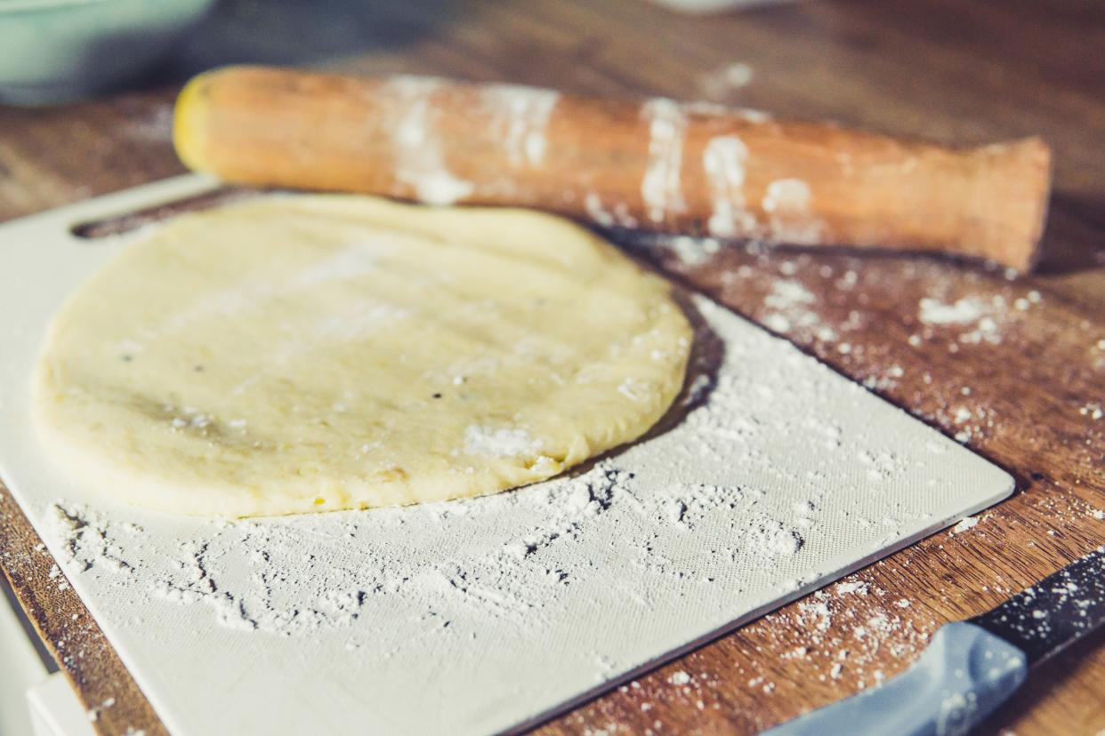 Round potato pizza dough with flour on a white cutting board with roller and knife on a rustic table with a blurred background