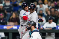 Boston Red Sox's Rafael Devers, right, celebrates his two-run home run with Enmanuel Valdez, left, next to Seattle Mariners catcher Cal Raleigh during the third inning of an opening-day baseball game Thursday, March 28, 2024, in Seattle. (AP Photo/Lindsey Wasson)