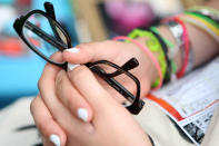 BERLIN, GERMANY - JULY 21: An attendee holds her pair of glasses at the second annual Hipster Olympics on July 21, 2012 in Berlin, Germany. With events such as the "Horn-Rimmed Glasses Throw," "Skinny Jeans Tug-O-War," "Vinyl Record Spinning Contest" and "Cloth Tote Sack Race," the Hipster Olympics both mocks and celebrates the Hipster subculture, which some critics claim could never be accurately defined and others that it never existed in the first place. The imprecise nature of determining what makes one a member means that the symptomatic elements of adherants to the group vary in each country, but the archetype of the version in Berlin, one of the more popular locations for those following its lifestyle, along with London and Brooklyn, includes a penchant for canvas tote bags, the carbonated yerba mate drink Club Mate, analogue film cameras, an asymetrical haircut, 80s neon fashion, and, allegedly, a heavy dose of irony. To some in Berlin, members of the hipster "movement" have replaced a former unwanted identity in gentrifying neighborhoods, the Yuppie, for targets of criticism, as landlords raise rents in the areas to which they relocate, particularly the up-and-coming neighborhood of Neukoelln. (Photo by Adam Berry/Getty Images)