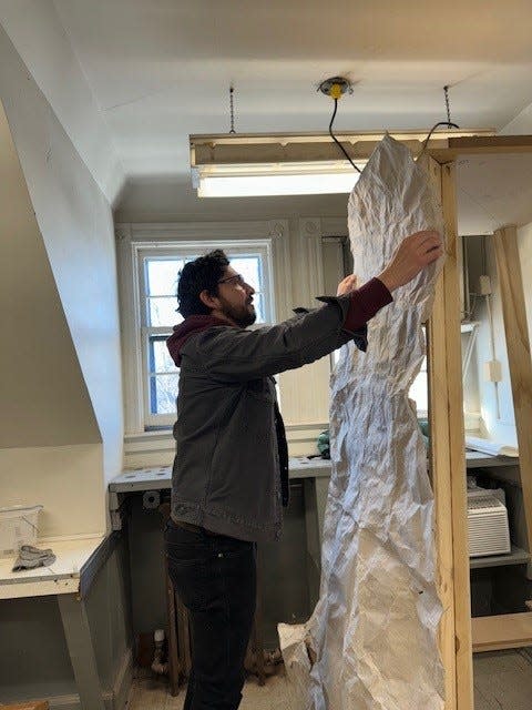 Pratt Munson artist-in-residence Felipe Lopez demonstrates how homemade hemp paper, cast from the Christopher Columbus monument on Memorial Parkway, will hang on a large wooden frame as part of his solo exhibition.