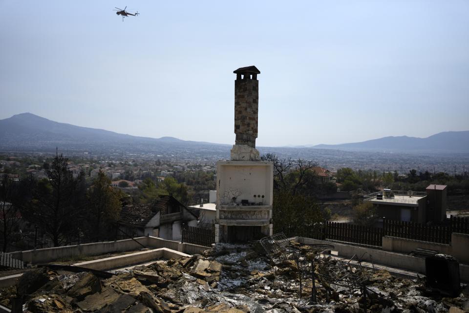 A helicopter flies near a burnt house in Acharnes suburb, on Mount Parnitha, in northwestern Athens, Greece, Thursday, Aug. 24, 2023. A major wildfire burning on the northwestern fringes of the Greek capital has torched homes and is now threatening the heart of a national park of Parnitha, one of the last green areas near the Greek capital. (AP Photo/Thanassis Stavrakis)