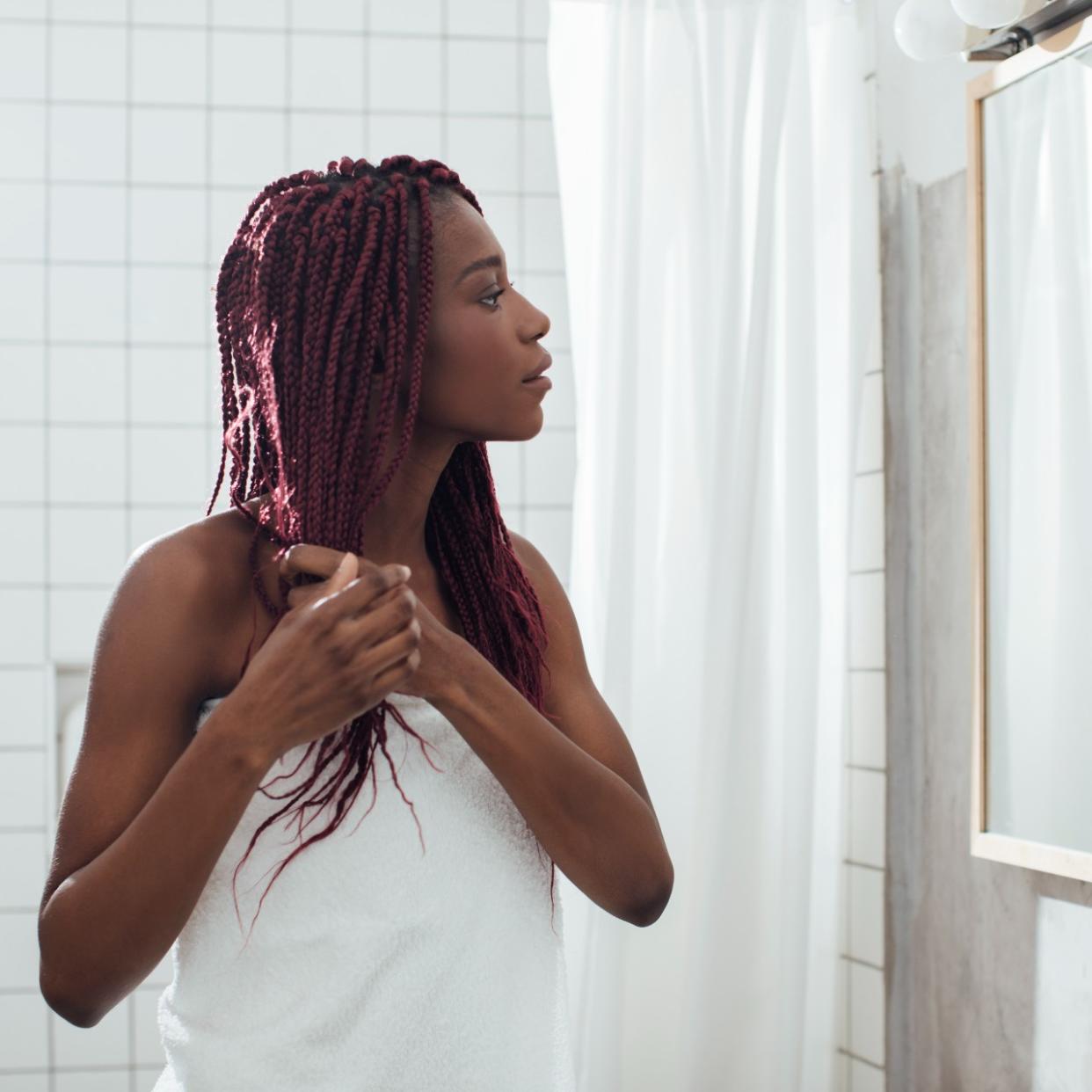  Young woman standing at bathroom and looking at mirror. while holding hair. 