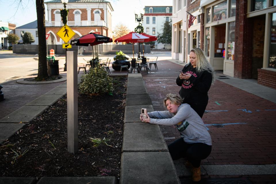 Paige Rossillo and Susie Monroe take photos of a mini monolith in a raised flowerbed on Hay Street on Tuesday, Dec. 8, 2020. The three foot tall sculpture first appeared on Thursday, Dec. 3, and nobody as yet taken credit for placing it there.
