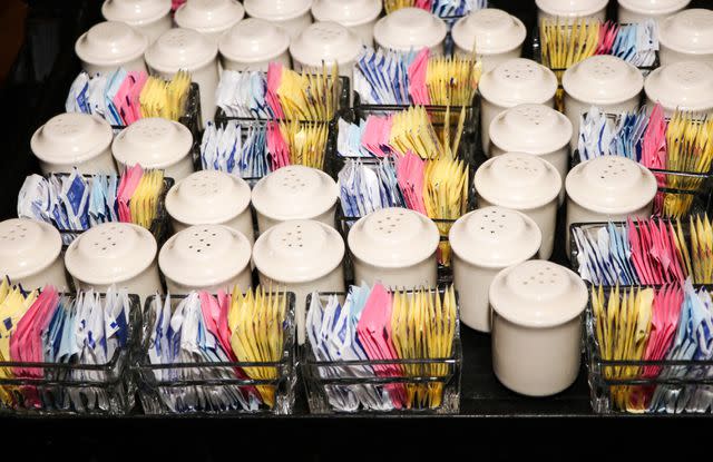 <p>Marie LaFauci / Getty Images</p> Food service tray with colorful sweetener packets, salt and pepper shakers.