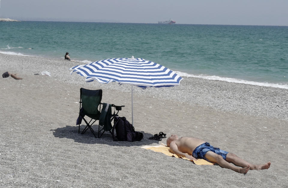 In this photo taken Monday, July 27, 2020, a man sunbathes on the beach with Turkey's research vessel, Oruc Reis, in the background, anchored off the coast of Antalya on the Mediterranean, Turkey. A top Turkish official said Tuesday that Turkey will suspend research for oil and gas exploration in disputed waters in the Eastern Mediterranean. President Recep Tayyip Erdogan told his aides to "be constructive and put this on hold for some time," presidential spokesman Ibrahim Kalin told Turkish broadcaster CNN Turk. (AP Photo/Burhan Ozbilici)