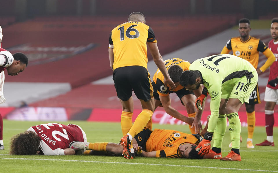 Players attend to Arsenal's David Luiz, left, and Wolverhampton Wanderers' Raul Jimenez following ahead clash during the English Premier League soccer match between Arsenal and Wolverhampton Wanderers at Emirates Stadium, London, Sunday, Nov. 29, 2020. (John Walton/Pool via AP)