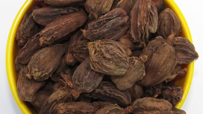 Top-down view of black cardamom seeds in a yellow bowl