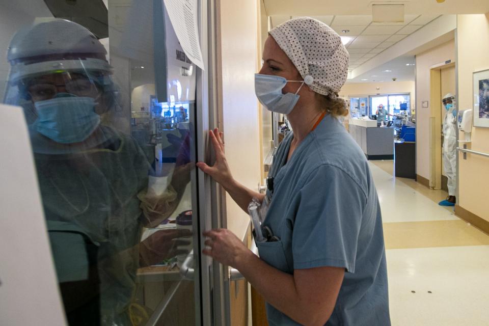 A nurse in a mask looks into the glass window of a hospital room