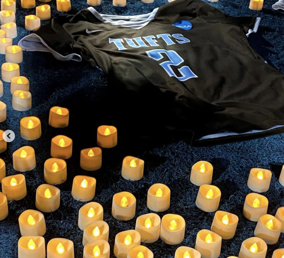 A black lacrosse jersey on the ground with 'Tufts' and '2' written in blue surrounded by candles. 