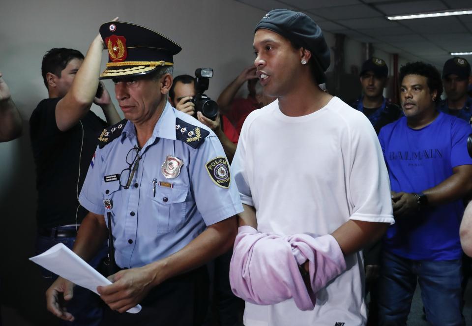 El ex astro brasileño de fútbol Ronaldinho camina esposado a una audiencia judicial en Asunción, Paraguay, el sábado, 27  de marzo del 2020. (AP Foto/Jorge Saenz)