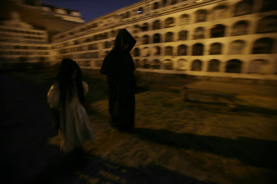 Guides walk under the moonlight at El Tejar cemetery, in downtown Quito, Ecuador, Wednesday, Sept. 11, 2019. The guides in black hooded capes lead tourists in the cemetery, navigating a maze of crypts as voices call out existential questions into the night. (AP Photo/Dolores Ochoa)