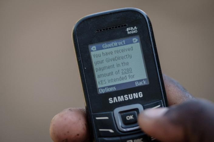 A villager shows his mobile phone's monitor displaying a message confirming the universal basic income transaction, 2,250 shillings per month ($22,19 euros) (AFP Photo/Yasuyoshi CHIBA)