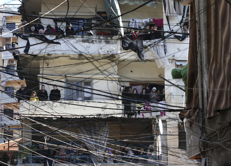 FILE - In this Jan. 11, 2015, file, photo, Alawite mourners seen through electricity wires stand on their balconies watching the funeral procession of those who were killed at a coffee shop where a suicide bombing struck, in the northern port city of Tripoli, Lebanon. Lebanon's energy minister said Thursday, July 16, 2020 the country's worsening economic crisis is making it increasingly difficult to attract investors for its ailing electricity sector.(AP Photo/Hussein Malla, File)