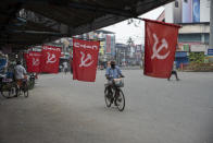 A man wearing mask as a precaution against COVID-19 pedals past flags of a Communist party trade union during a nation wide strike by various trade unions in Kochi, Kerala state, India, Thursday, Nov. 26, 2020. India has more than 9 million cases of coronavirus, second behind the United States. (AP Photo/R S Iyer)
