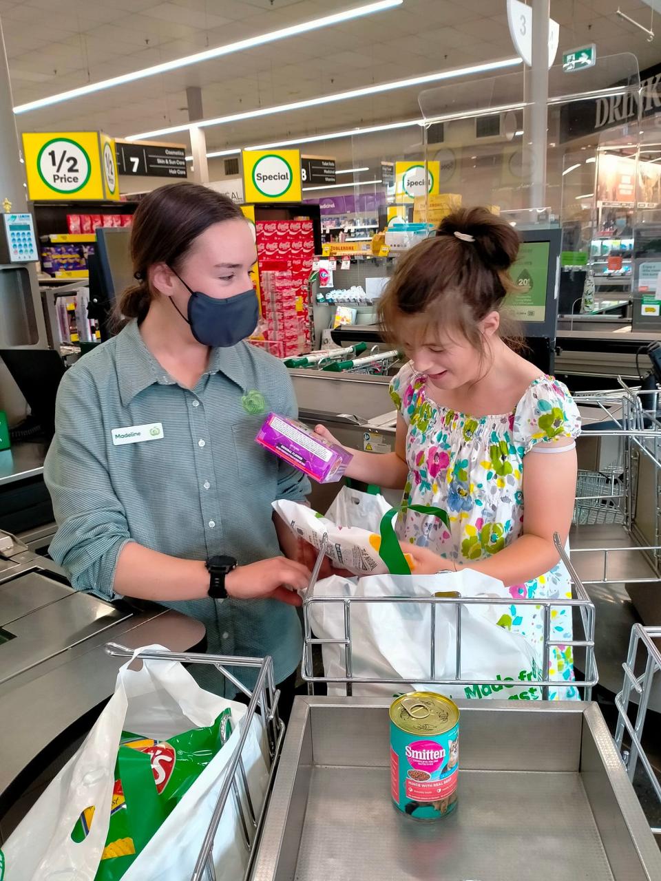 Woolworths worker on left speaking to adolescent girl on right as they pack groceries together behind the counter. Source: Facebook/Bella Jade