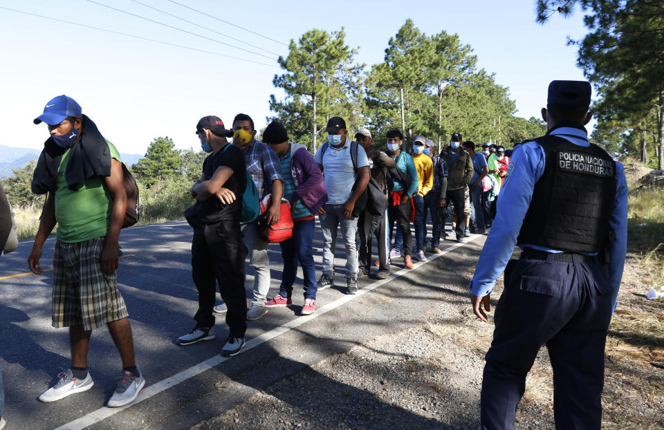 Migrants line up at a police checkpoint on their way North near Agua Caliente, close to the border with Guatemala, Thursday, Dec. 10, 2020. Honduran security forces stationed on the highway a few kilometers before Agua Caliente, asked the migrants for their passports or identity cards and proof of a COVID-19 test, and if they did not produce those documents they would not be allowed to move on. (AP Photo/Delmer Martinez)