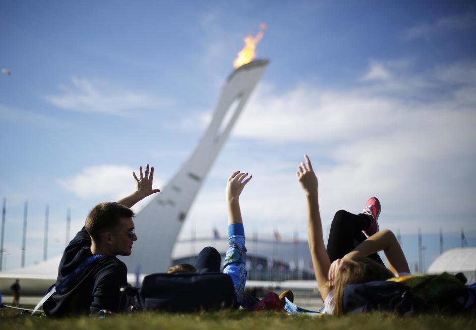 In this Wednesday, Feb. 12, 2014, photo, volunteers from left, Vladimir Malakhov, Elena Ripenko, and Aleksandra Zhuk, lay out on the lawn under the Olympic cauldron at the 2014 Winter Olympics, in Sochi, Russia. Temperatures were near 60 degrees Fahrenheit in Sochi on Wednesday. (AP Photo/David Goldman)