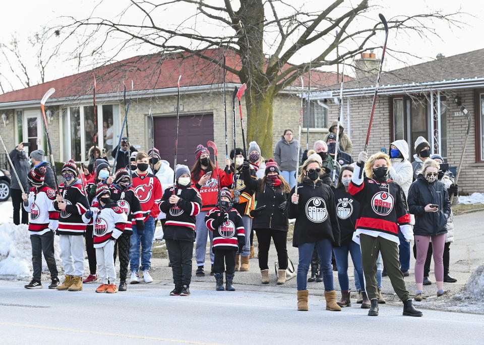 People lift hockey sticks to pay their respects across the street where Walter Gretzky's funeral service was being held in Brantford, Ontario, on Saturday, March 6, 2021. Walter Gretzky also know as Canada's hockey dad was 82 years old. (Nathan Denette/The Canadian Press via AP)