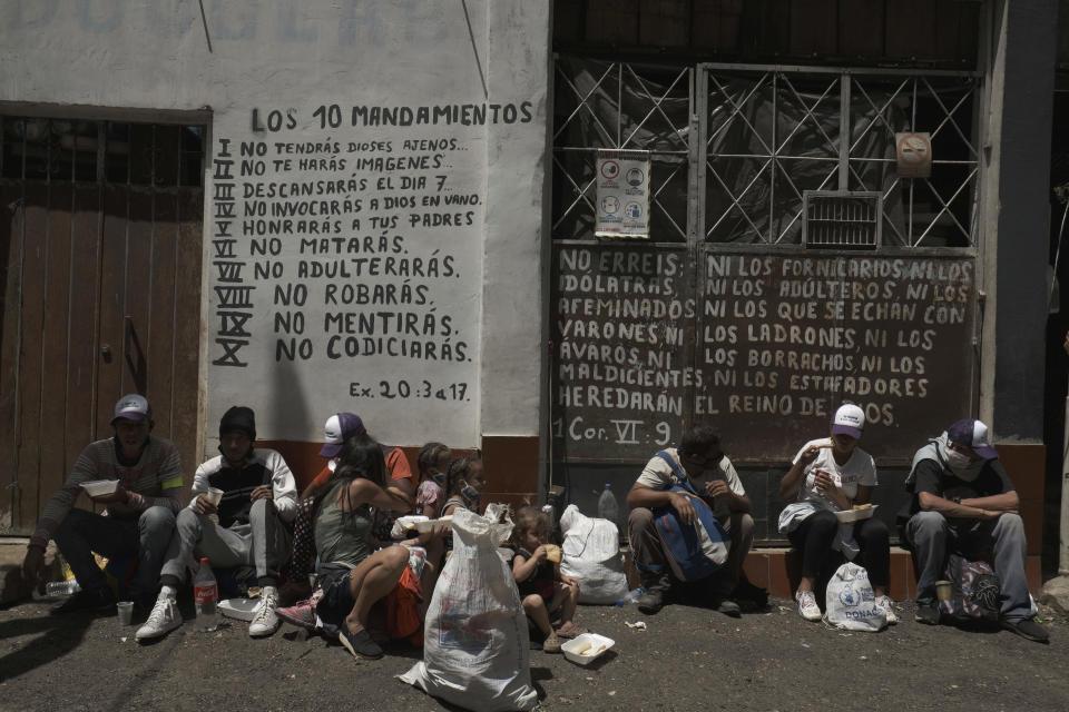 Venezuelan migrants rest as they receive free food, in front of passages from the Bible in Pamplona, Colombia, Wednesday, Oct. 7, 2020, a few hours by car from the Venezuelan border. Amid COVID-19, shelters remain closed, drivers are more reluctant to pick up hitchhikers, and locals who fear contagion are less likely to help out with food donations. (AP Photo/Ferley Ospina)