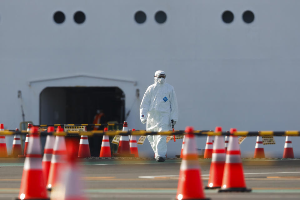 A man wearing a protective suit walks near the quarantined Diamond Princess cruise ship Wednesday, Feb. 19, 2020, in Yokohama, near Tokyo. Passengers tested negative for COVID-19 will start disembarking Wednesday. (AP Photo/Jae C. Hong)