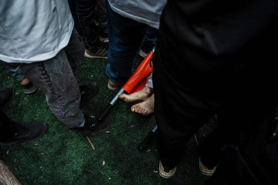 People stand near a litter holding a body. All but the bare feet of the body are obscured by mourners.