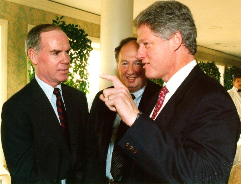 Three men in dark suits stand together and talk.