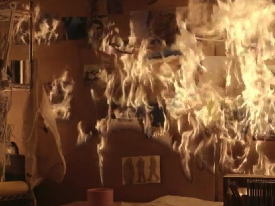 a desk, lamp, and collection of some drawings of a spaceman on the wall, all lit on fire in the poolhouse in "Station eleven"