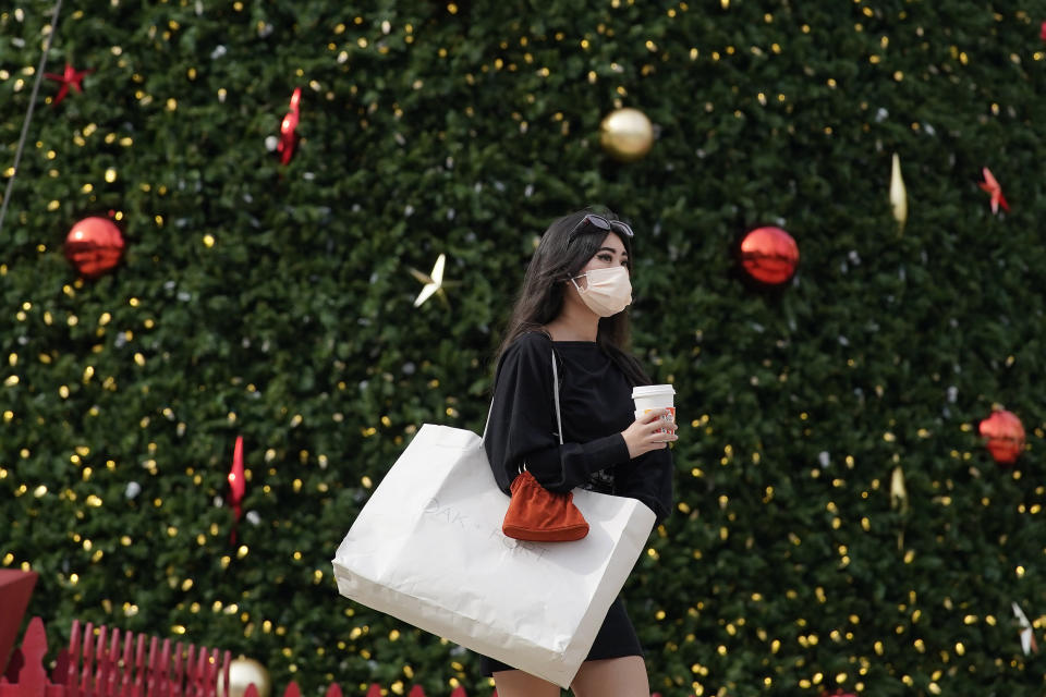 A woman wears a mask as she carries a shopping bag in front of the annual Macy's Great Tree at Union Square during the coronavirus outbreak in San Francisco, Saturday, Nov. 21, 2020. (AP Photo/Jeff Chiu)