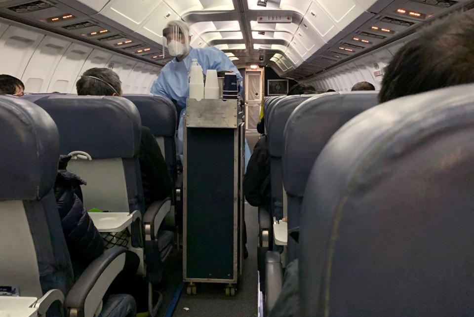 A Flight attendant wearing protective clothing and a mask serves snacks to Canadians, who had been evacuated from China due to the outbreak of novel Coronavirus on an American charter plane, on another aircraft taking them to Canadian Forces Base (CFB) Trenton, from Vancouver International Airport in Richmond, British Columbia, Canada February 7, 2020.  Courtesy of Edward Wang via REUTERS. THIS IMAGE HAS BEEN SUPPLIED BY A THIRD PARTY. MANDATORY CREDIT