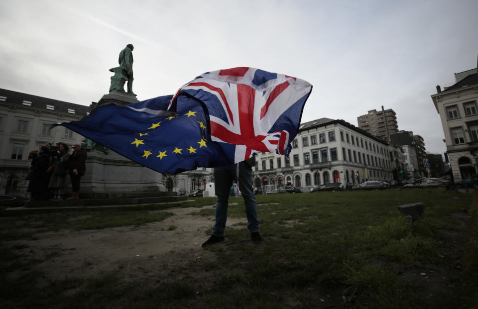 FILE - In this Thursday, Jan. 30, 2020 file photo, a man unfurls a Union and EU flag outside the European Parliament in Brussels. Britain and the European Union have struck a provisional free-trade agreement that should avert New Year chaos for cross-border traders and bring a measure of certainty for businesses after years of Brexit turmoil. (AP Photo/Virginia Mayo, File)