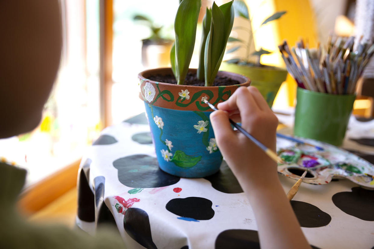 Over the shoulder view of a child painting a terracotta plant pot with bright coloured paints on a dining table in springtime. (Elva Etienne / Getty Images stock)