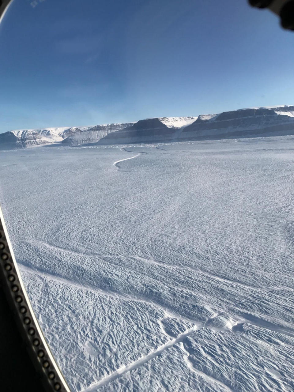 A portion of the new rift at the center of Petermann Glacier's floating ice shelf (straight feature near bottom center), and an older rift from the side of the shelf (near top center), as photographed during a recent Operation IceBridge mission in northeast Greenland. <cite>Kelly Brunt/NASA</cite>