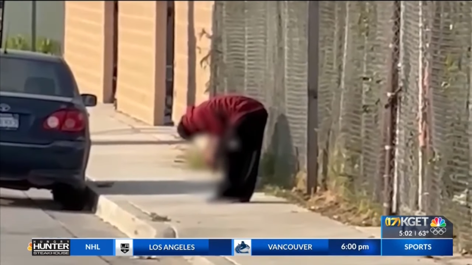 A person appears to defy gravity, leaning at a steep angle on a sidewalk next to a fence