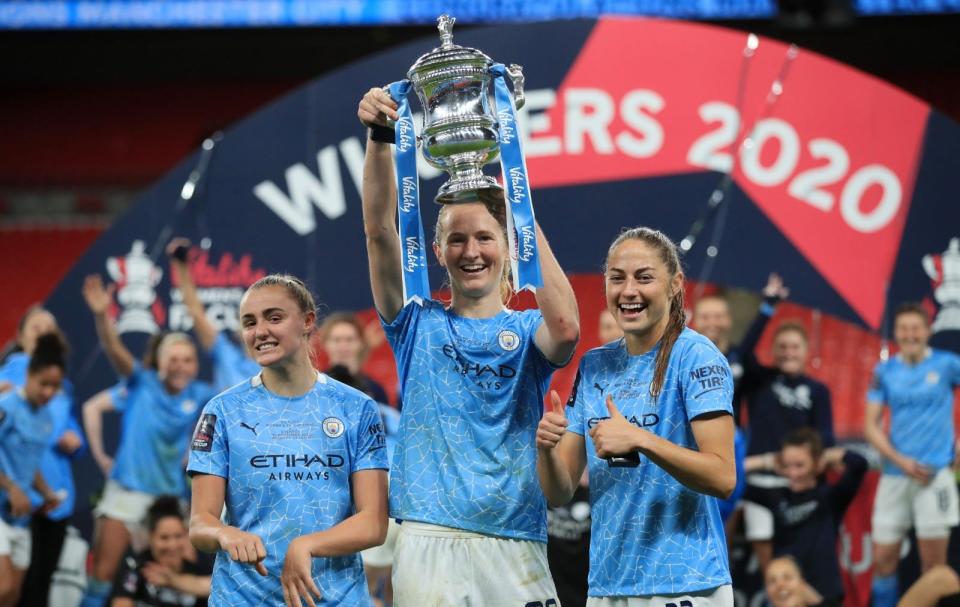 Sam Mewis raises the Women's FA Cup trophy following Manchester City's 3-1 win over Everton at Wembley Stadium in London on Sunday, Nov. 1, 2020. Mewis is flanked by teammates Georgia Stanway, left, and Janine Beckie.