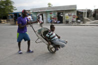 In this Dec. 3, 2019 photo, a young man pushes a wheelbarrow home as his little brother takes a ride on it, in the Cite Soleil slum of Port-au-Prince, Haiti. The two youths are going home after helping their mother by carrying items to sell in the market. In the last two years, Haiti’s currency, the gourde, declined 60% against the dollar and inflation recently reached 20%. (AP Photo/Dieu Nalio Chery)