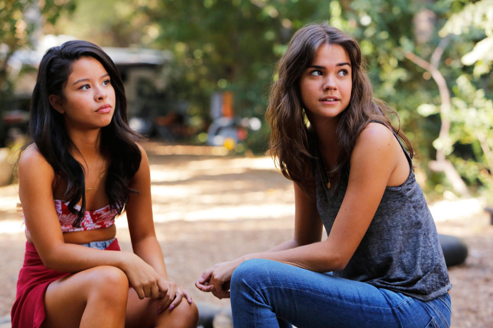 Cierra Ramirez and Maia Mitchell are seated outdoors, engaging in conversation. Cierra wears a cropped top and skirt; Maia wears a sleeveless top and jeans