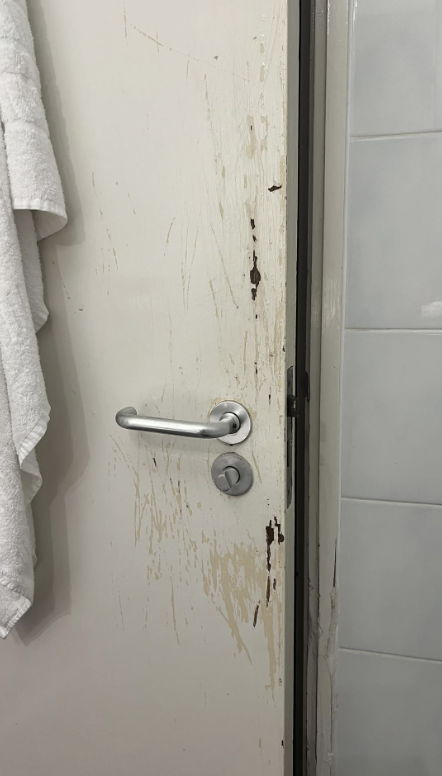 A bathroom door with several scratches and chipped paint around the handle. A white towel hangs to the left