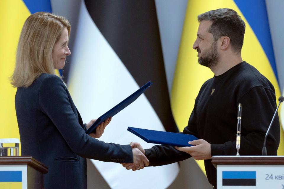 Ukrainian President Volodymyr Zelenskyy and Estonia's Prime Minister Kaja Kallas shake hands and exchange documents