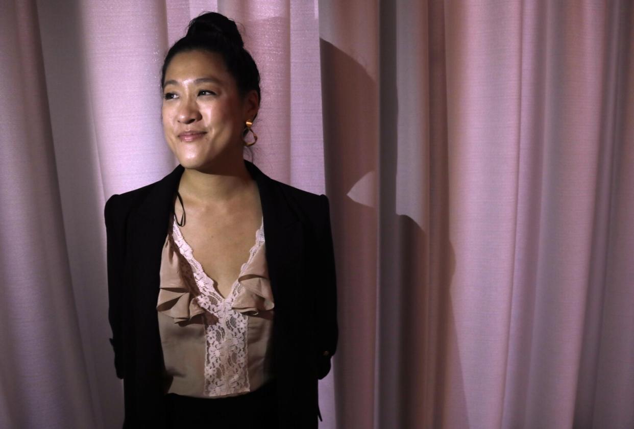 A woman stands in front of a pink curtain.