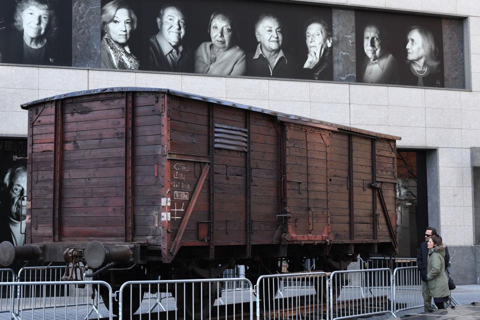 Portraits of Holocaust survivors are displayed in April 2019 at New York's Museum of Jewish Heritage, as a vintage German train car, like those used to transport people to Auschwitz and other Nazi death camps, is seen in front of the building. (Photo: TIMOTHY A. CLARY via Getty Images)