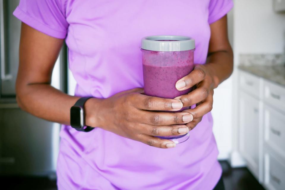 A woman holds a blueberry smoothie.