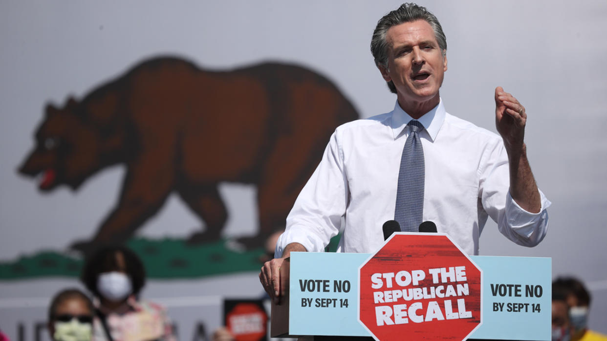 California Gov. Gavin Newsom stands at a podium with a sign reading: Vote no by Sept. 14, Stop the Republican recall.