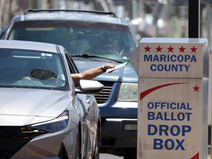 یک رای دهنده در 02 اوت 2022 در فینیکس، آریزونا، یک برگه رای را در یک جعبه در بیرون از بخش انتخابات شهرستان ماریکوپا قرار می دهد.