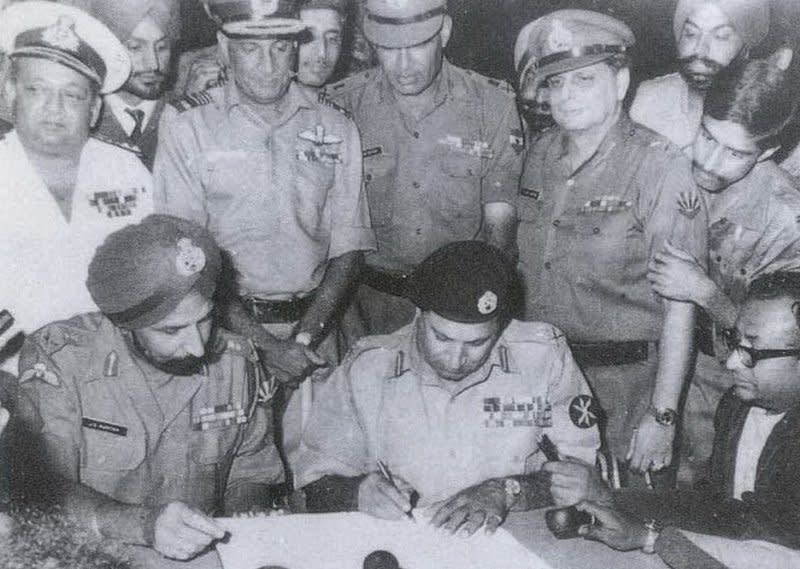 Pakistan's Lt. Gen. A.A.K. Niazi (sitting, center) signs the Pakistani Instrument of Surrender under the gaze of Indian Lt. Gen. Jagjit Singh Aurora (sitting, left) in Dhaka, Bangladesh, on December 16, 1971. The ceremony marked the end of the Bangladesh Liberation War, giving Bangladesh independence. Also attending are, standing, from left, Vice Adm. Krishnan, Air Marshal Dwan, Lt. Gen Sagat Singh, Maj. Gen. JFR Jacob and Flt. Lt. Krishnamurthy. Sitting, right, is Surojit Sen, a newscaster from All India Radio. File Photo courtesy of the Indian Navy