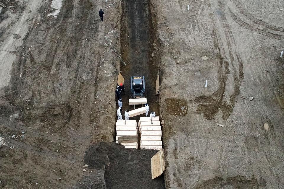 Workers wearing personal protective equipment bury bodies in a trench on Hart Island, April 9, 2020.