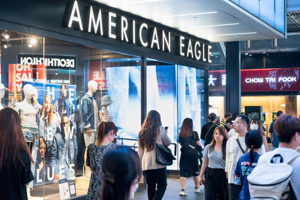 People walk past an American Eagle clothing store with mannequins in the display window on a busy city street