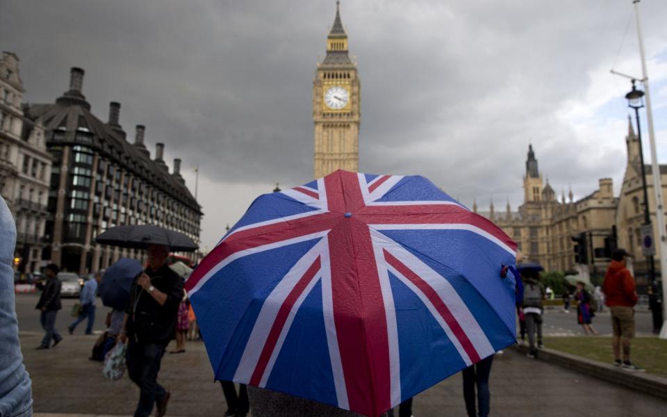 A pedestrian sheltering from the rain beneath a Union flag themed umbrella as they walk near the Big Ben clock face in central London on June 25, 2016, following the pro-Brexit result - AFP