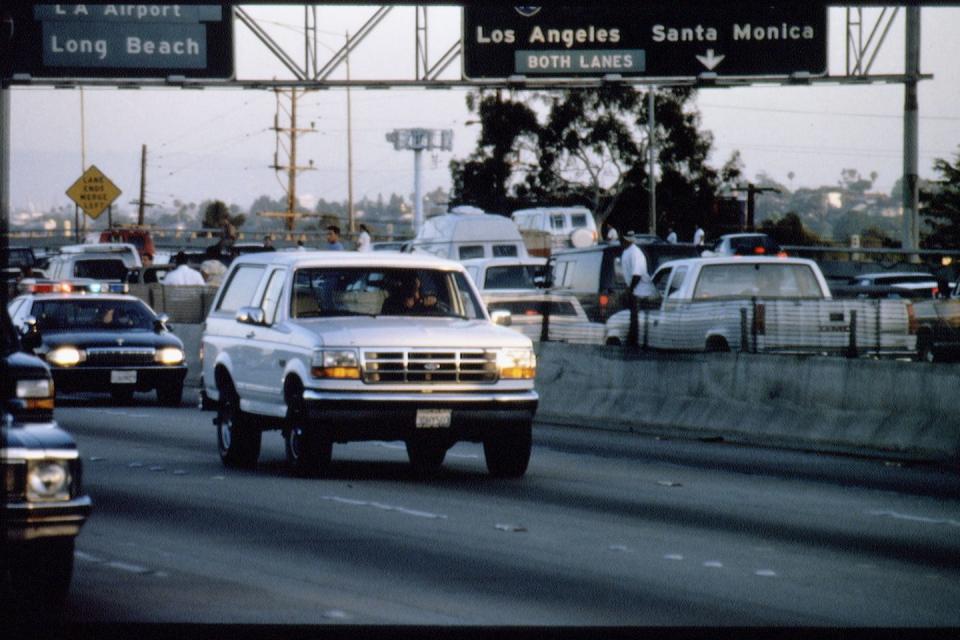 a white car driving on a highway followed by police cars